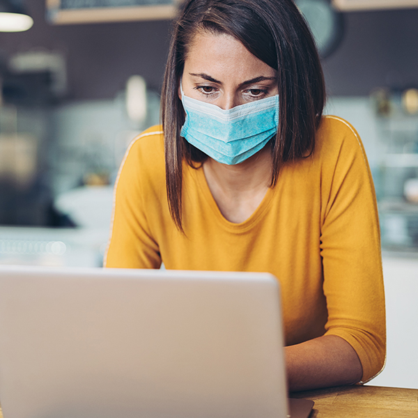 A woman with a mask consults her laptop inside a place of business.