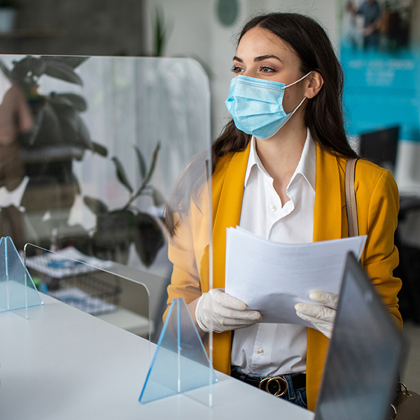 A masked man behind a clear partition helps a masked customer.