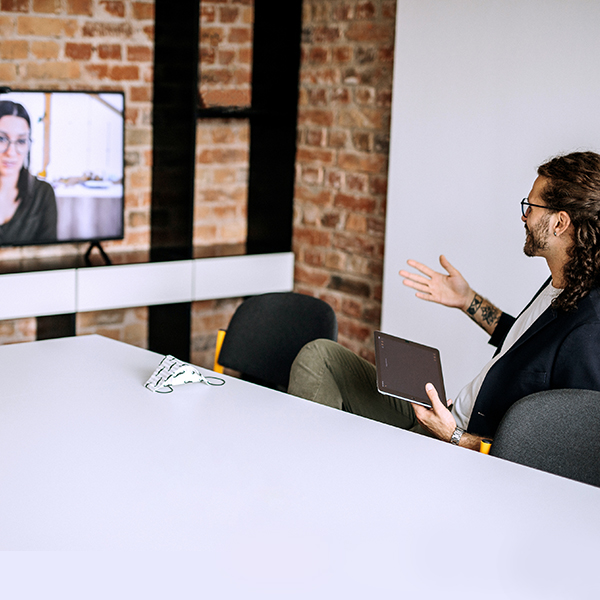 A man holding a tablet has a virtual meeting with a woman.