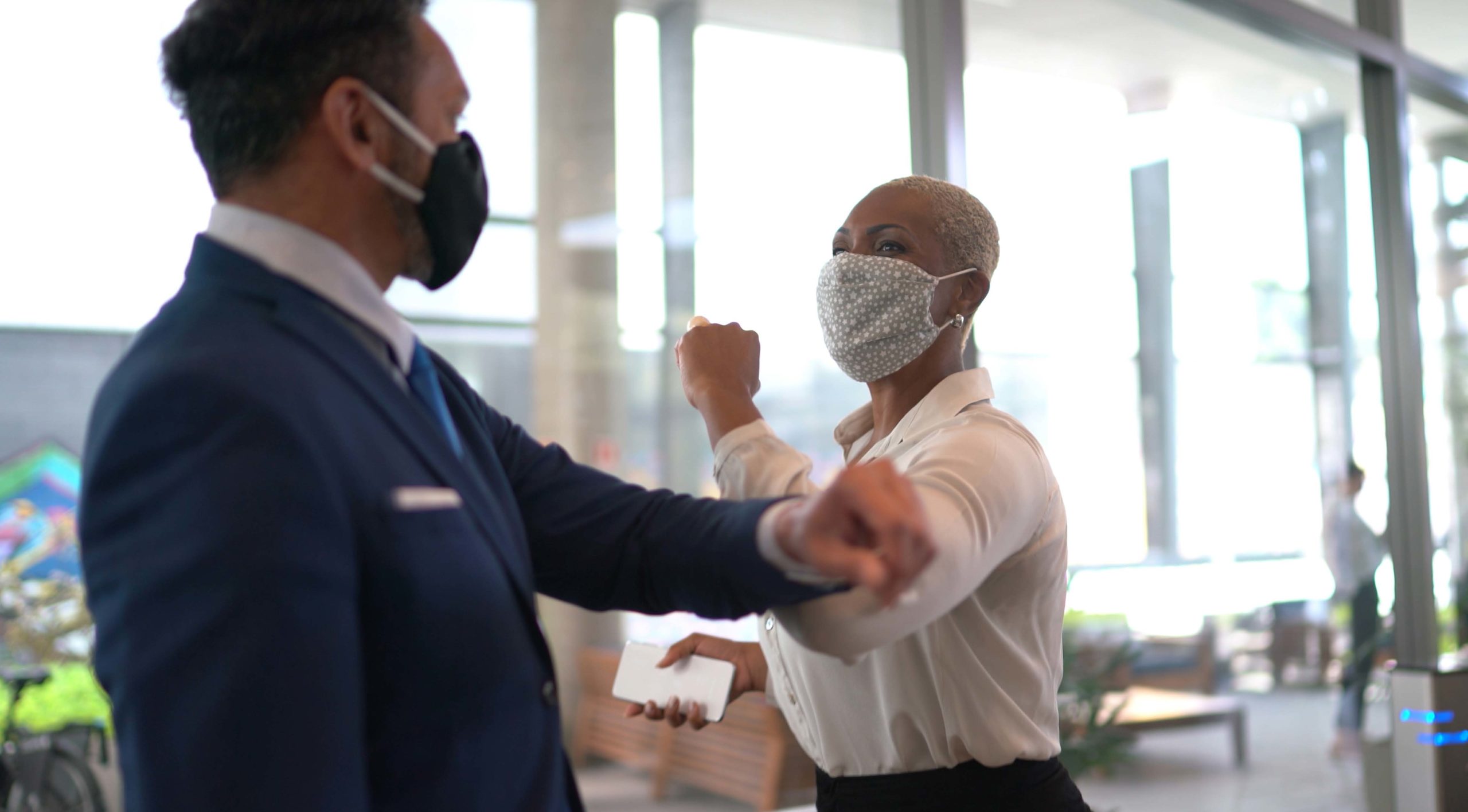 A man “elbow bumps” a woman. Both are masked.