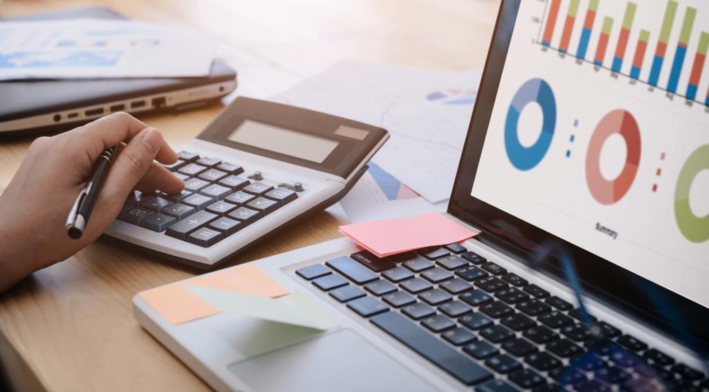 A close-up shot of someone working at a desk with a calculator and a laptop.