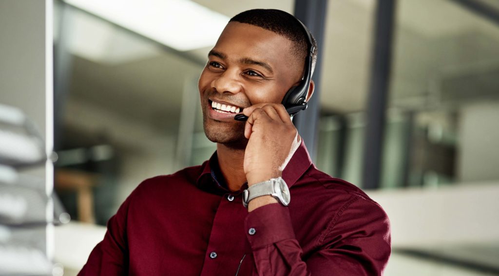 A smiling man talks into a headset.