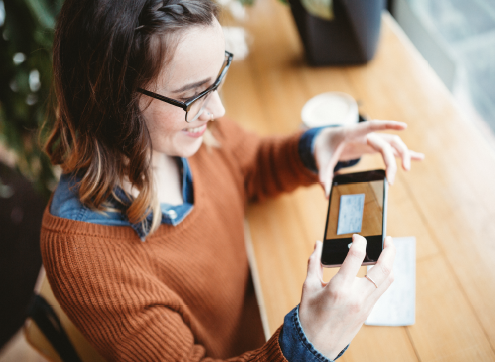 A woman smiles as she takes a digital image of a check.