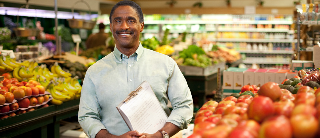 A business owner holds a clipboard in their grocery store.