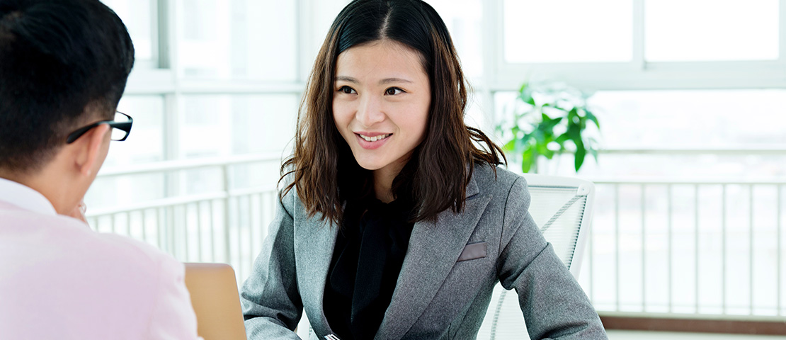 A woman in front of an open laptop smiles as she takes notes during a meeting.