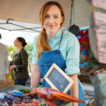 A woman wearing an apron sells lobsters at an outdoor market.