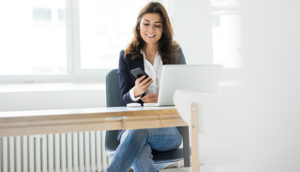 A woman sitting down with a laptop and holding a mobile phone
