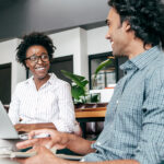 A man and woman smile at one another in an office setting.