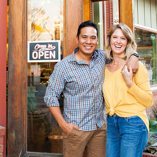 A man and woman smile next to each other in front of their small business.