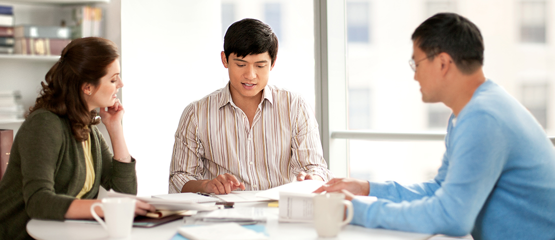 Three people sit at a table, reviewing paperwork.